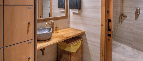 A bathroom with wooden cabinets, a sink, a mirror, a shower, and a towel dispenser.