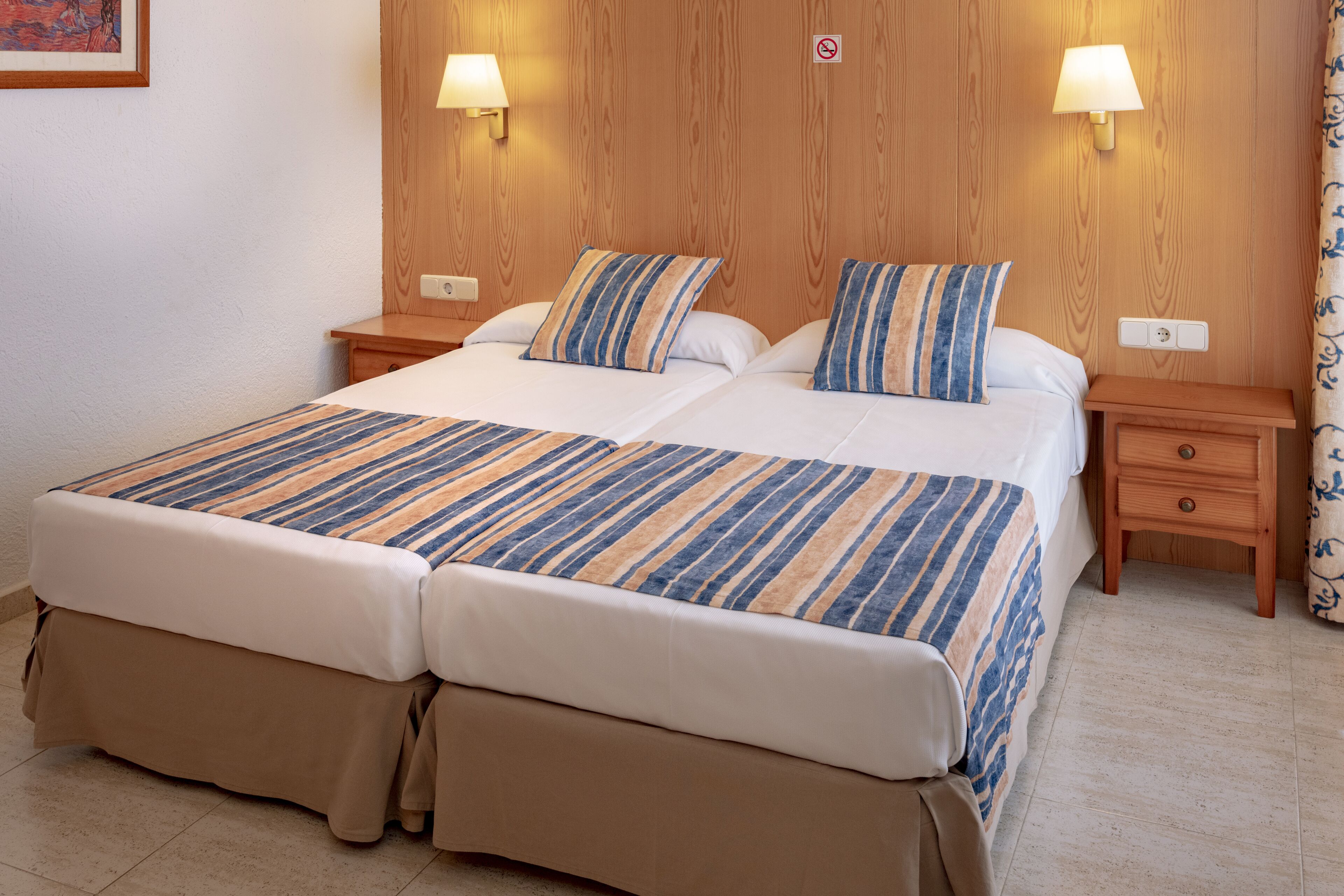 A double bed with striped bedding, two bedside tables with lamps, and a wooden headboard.