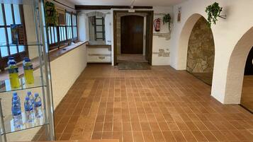 A spacious hallway with tiled flooring, a glass display case with water bottles, a wooden door, and stone arches.