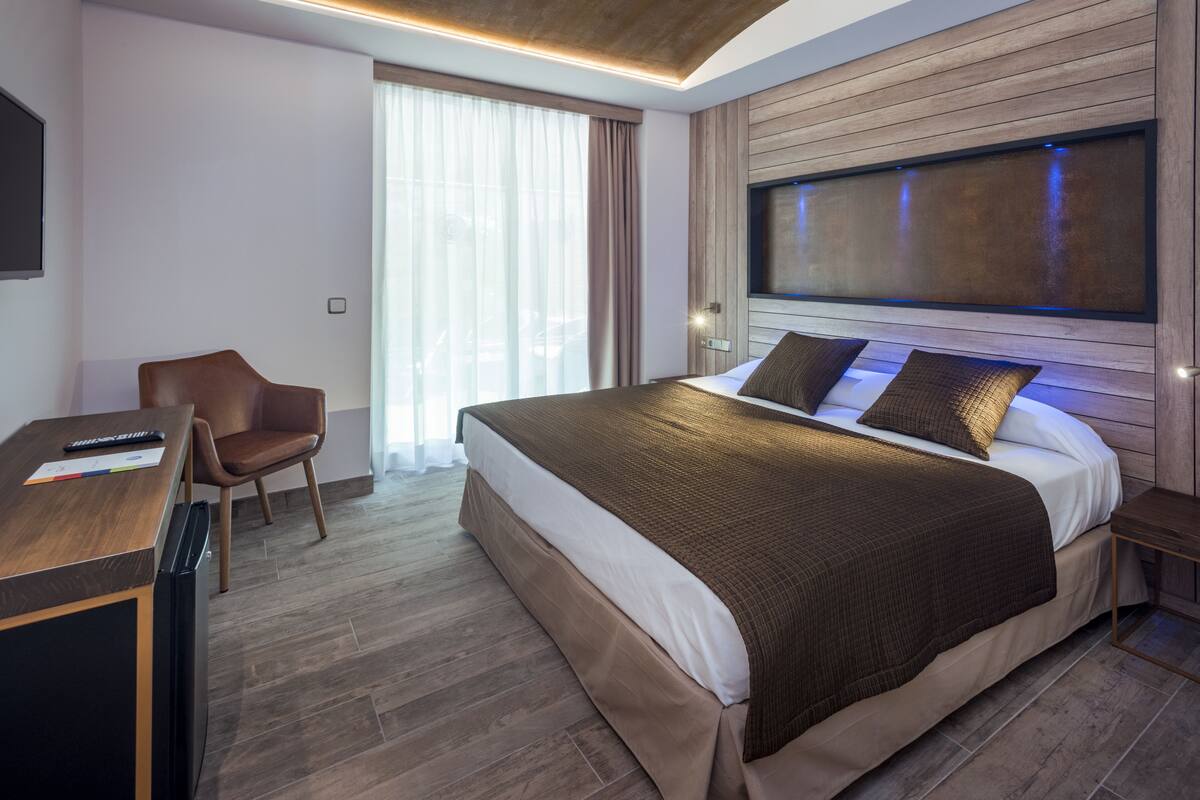A modern hotel room with a large bed, a desk, a chair, and a TV mounted on the wall.
