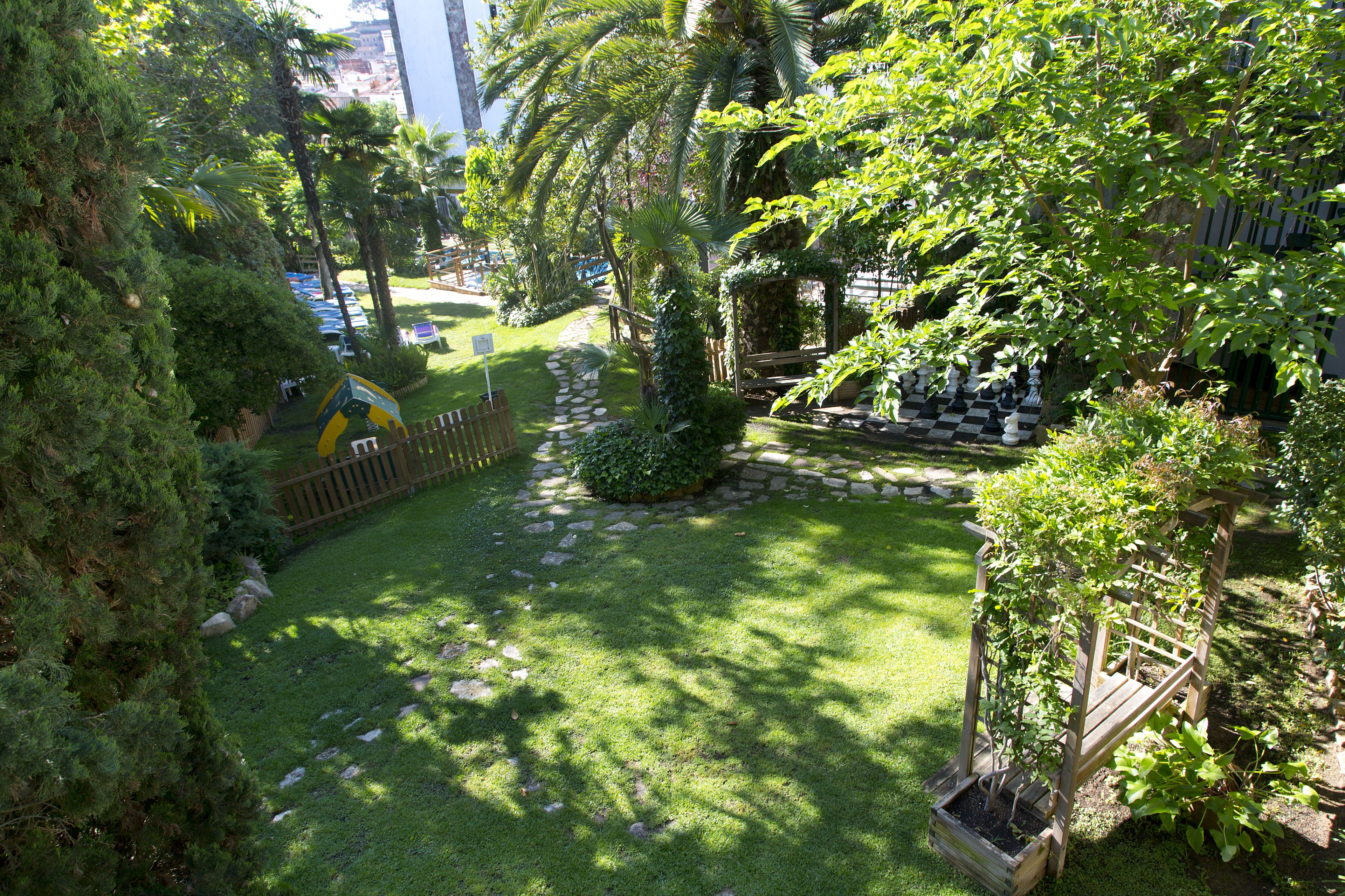 Un jardín bien cuidado con un sendero de piedra, abundante vegetación y un banco de madera.