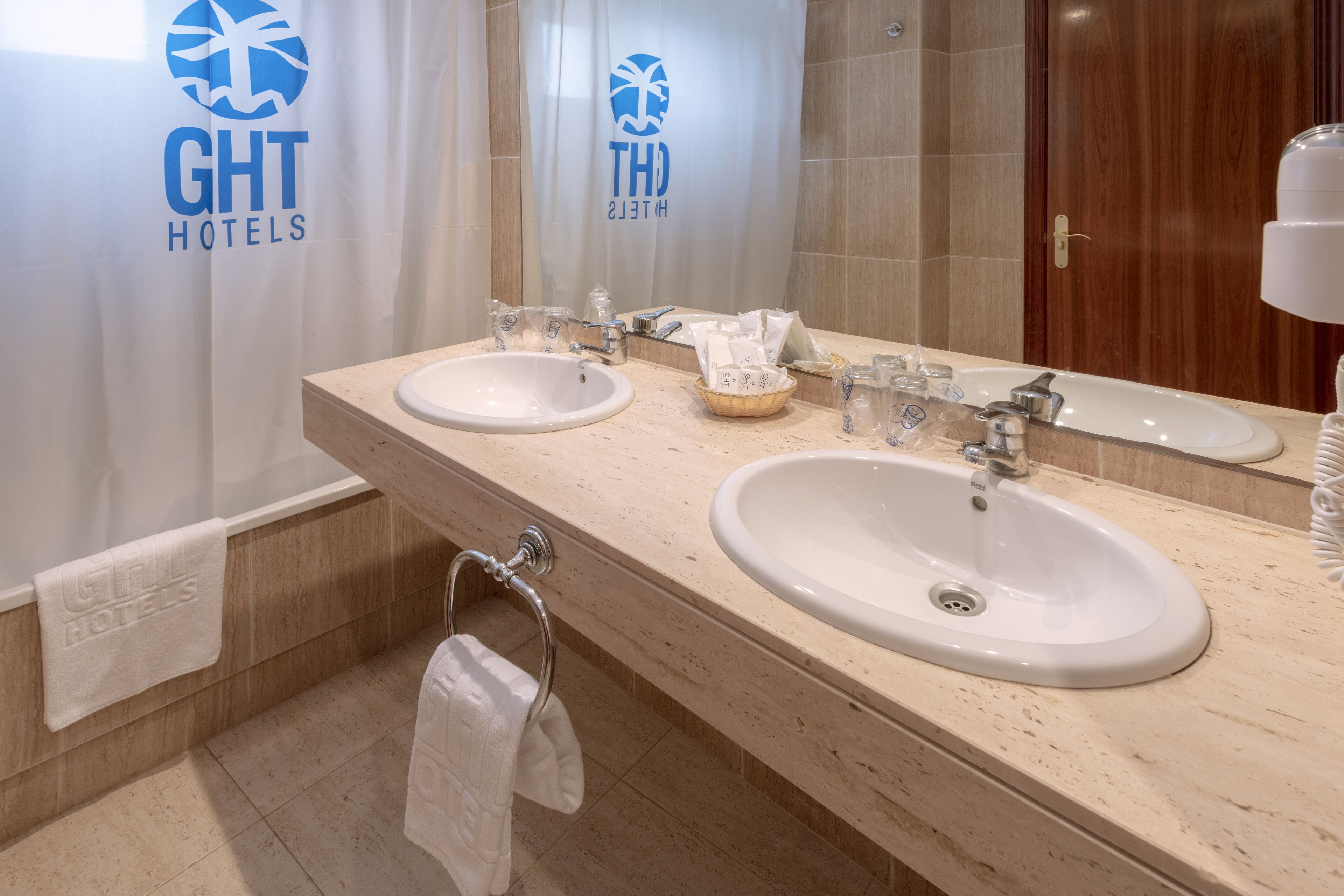 A hotel bathroom with two sinks, a mirror, and a towel rack.
