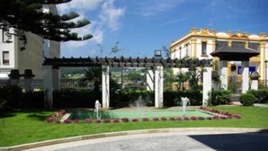 A garden with a fountain, a pergola, and a building with classical architecture. - Palacio Arias & Hotel y Apartamentos Arias (Navia)