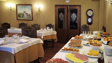 Un comedor con varias mesas dispuestas para el desayuno, mostrando una variedad de alimentos y un reloj en la pared.