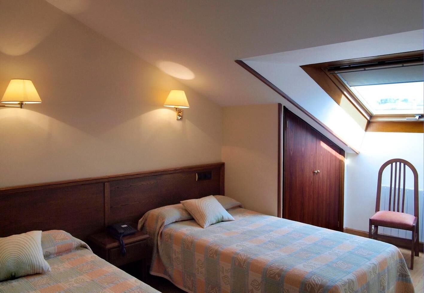 Habitación de hotel con dos camas, un escritorio con teléfono, una silla y un armario.