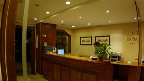 A reception desk with a wooden finish, a computer, and a plant. There are framed pictures on the wall and a sign with a rating. - Palacio Arias & Hotel y Apartamentos Arias (Navia)