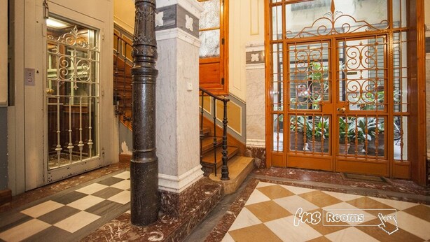 Un vestíbulo de hotel con suelo a cuadros, una escalera y una puerta de madera grande con paneles de vidrio.