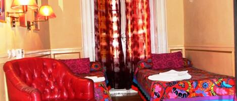 Una habitación con dos camas, un sillón rojo y un ventilador de techo.