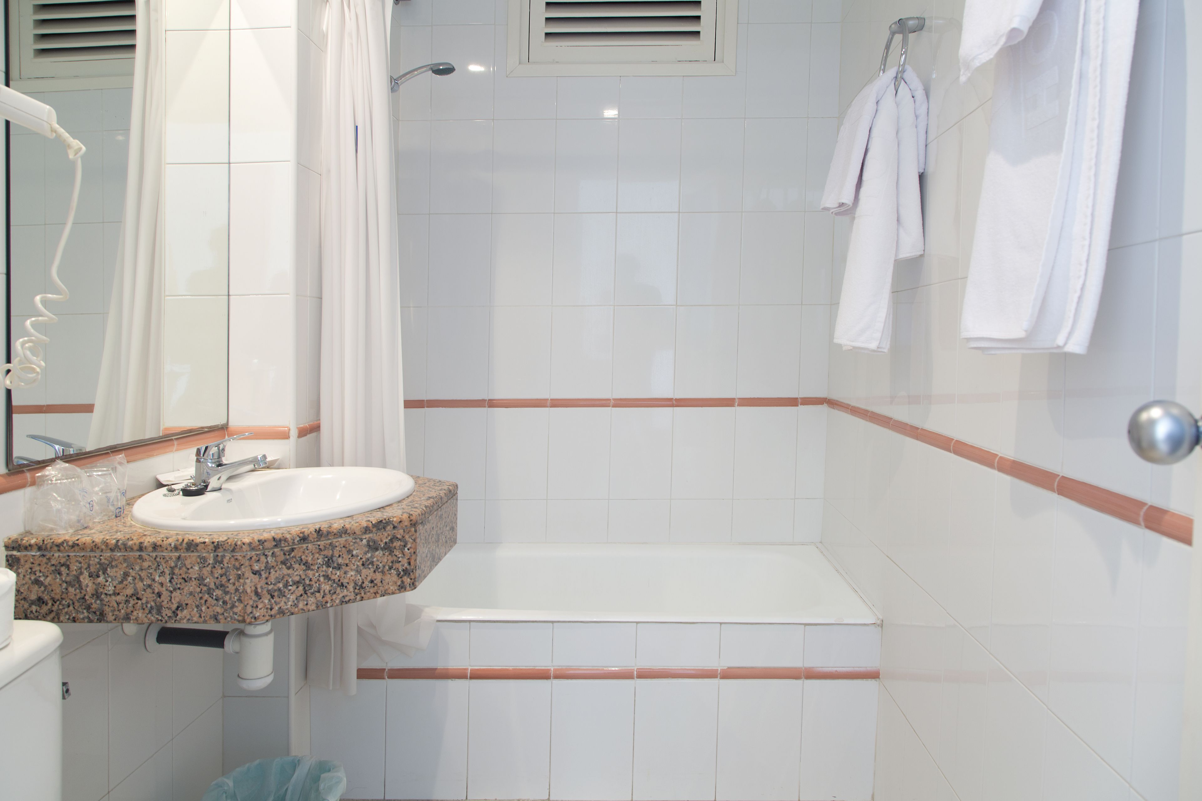 Un baño con lavamanos de granito, bañera blanca y cortina de ducha.