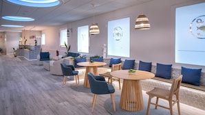 A modern hotel lobby with round tables, blue chairs, and a reception desk. - GHT Balmes, Hotel, Aparthotel & SPLASH (Calella)