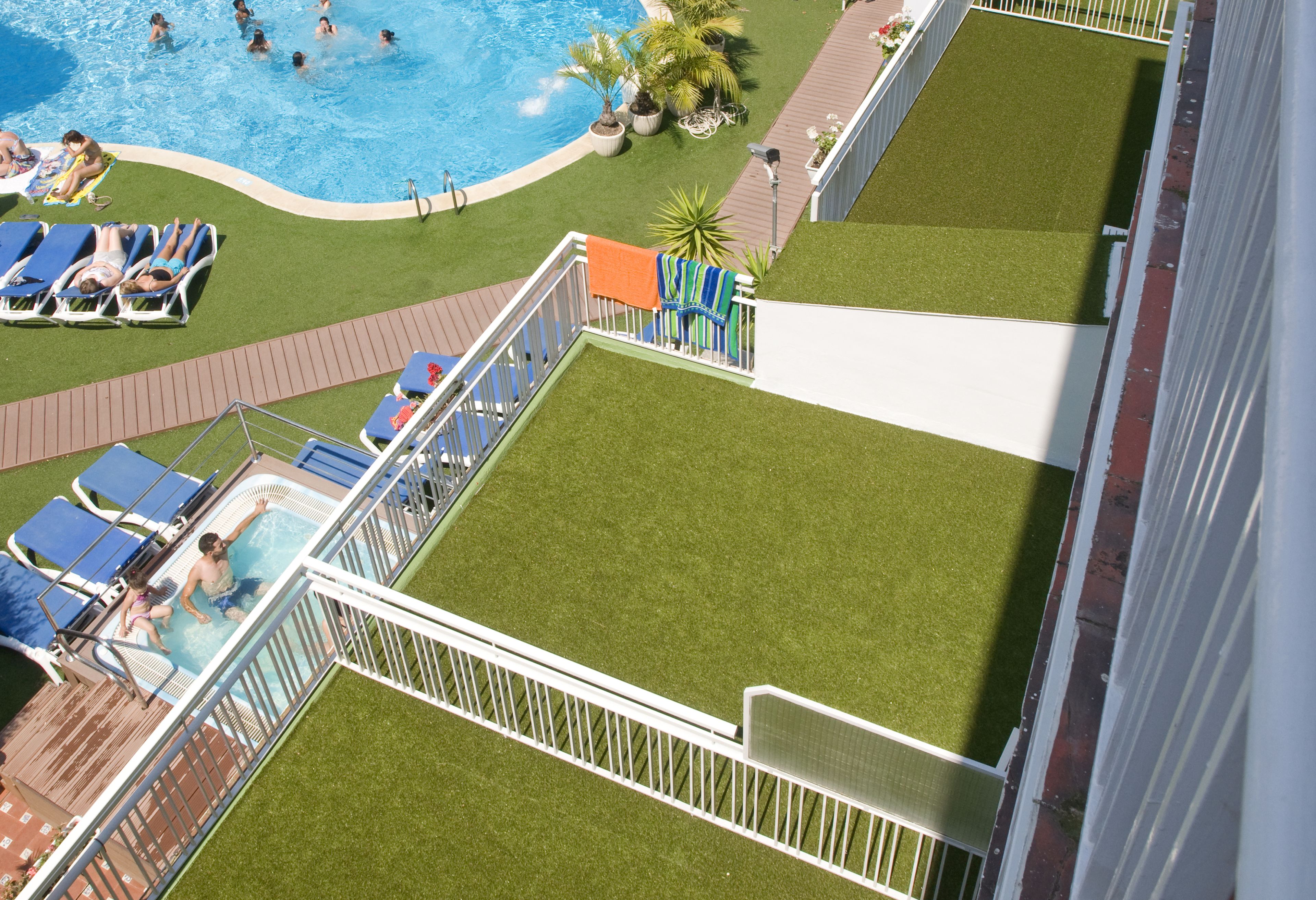 Uma área de piscina no terraço, com várias piscinas, espreguiçadeiras e um deck gramado.