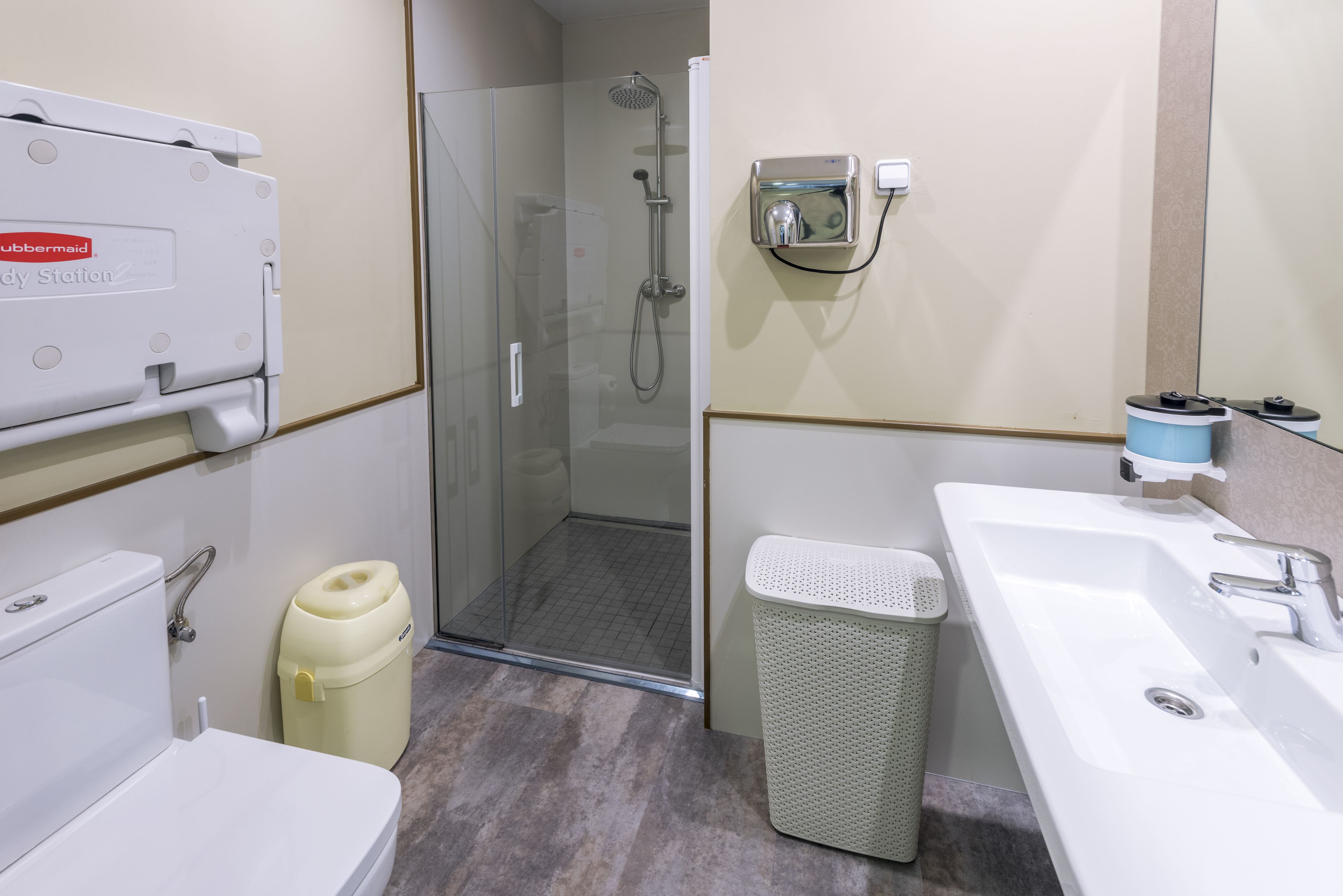 Baño con inodoro, lavabo, ducha y cubo de basura.