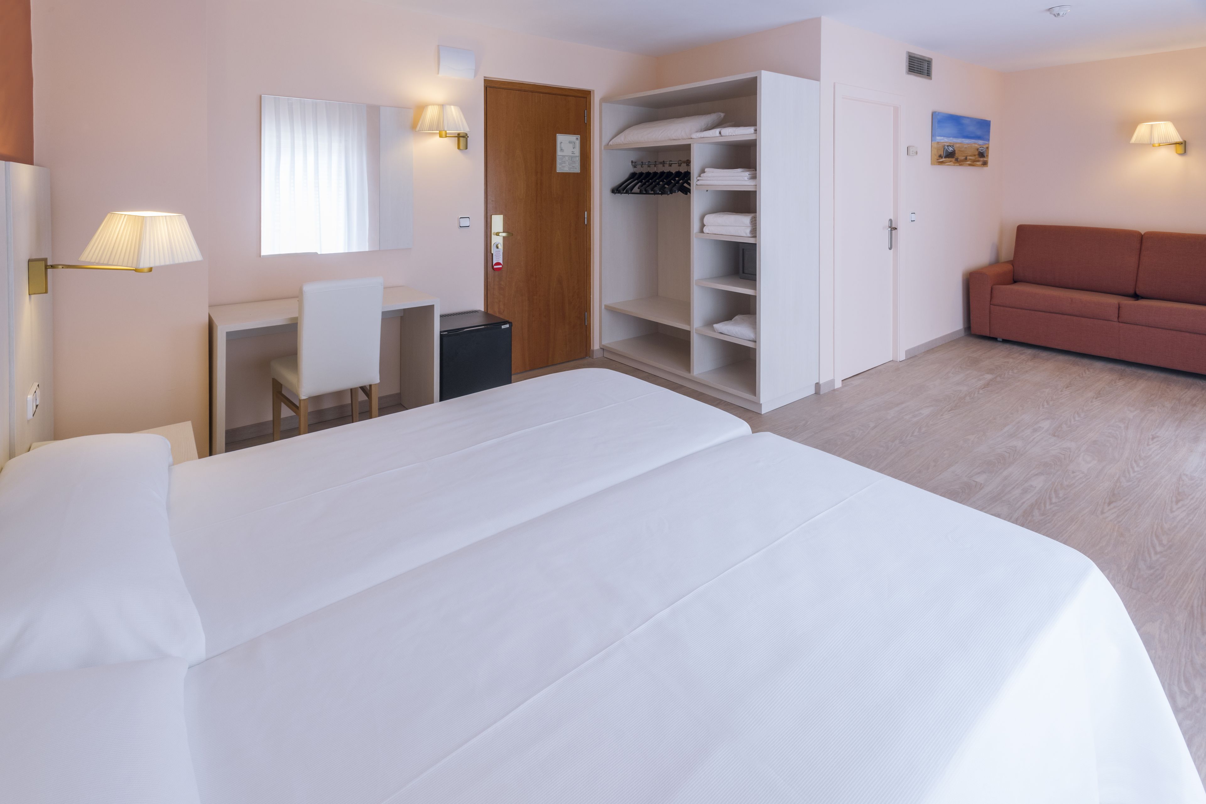 Una habitación de hotel con cama, escritorio, silla, armario y sofá.