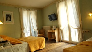 A room with two beds, a desk, a chair, a television, and a window with curtains. - Hôtel de France (Béziers)