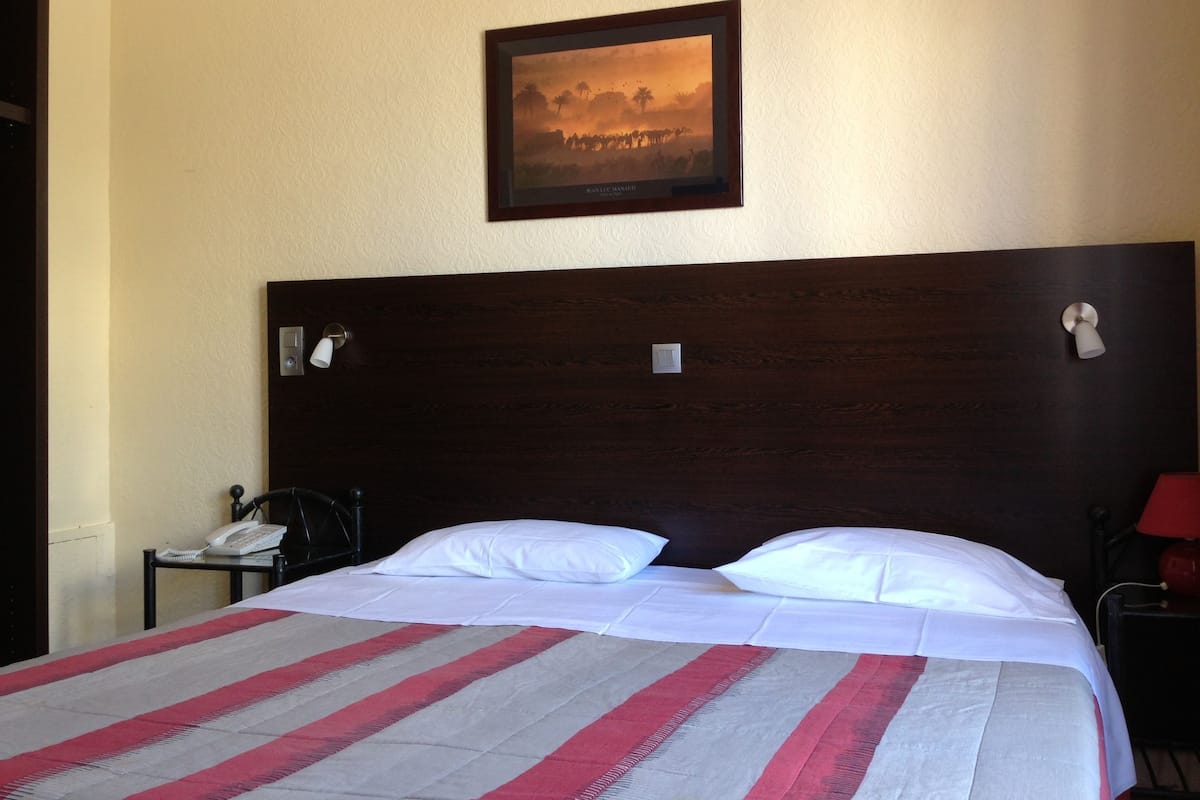 A hotel room with a large bed, a nightstand, a telephone, and a framed picture on the wall.