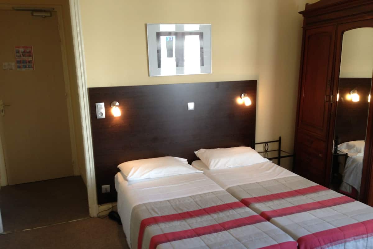 A hotel room with two beds, a wooden headboard, a mirror, and a wall-mounted light fixture.