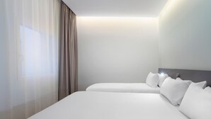Een hotelkamer met twee bedden, een groot raam met dunne gordijnen en een bedlampje.