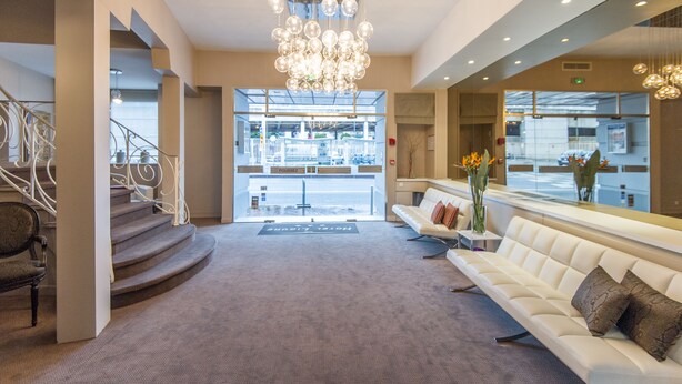 A hotel lobby with a staircase, a chandelier, a reception desk, and a seating area. - Ligure Cannes (Cannes)