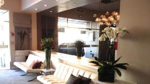 A modern reception area with a white reception desk, a seating area with a sofa and chairs, and a large window providing a view of the street. - Ligure Cannes (Cannes)