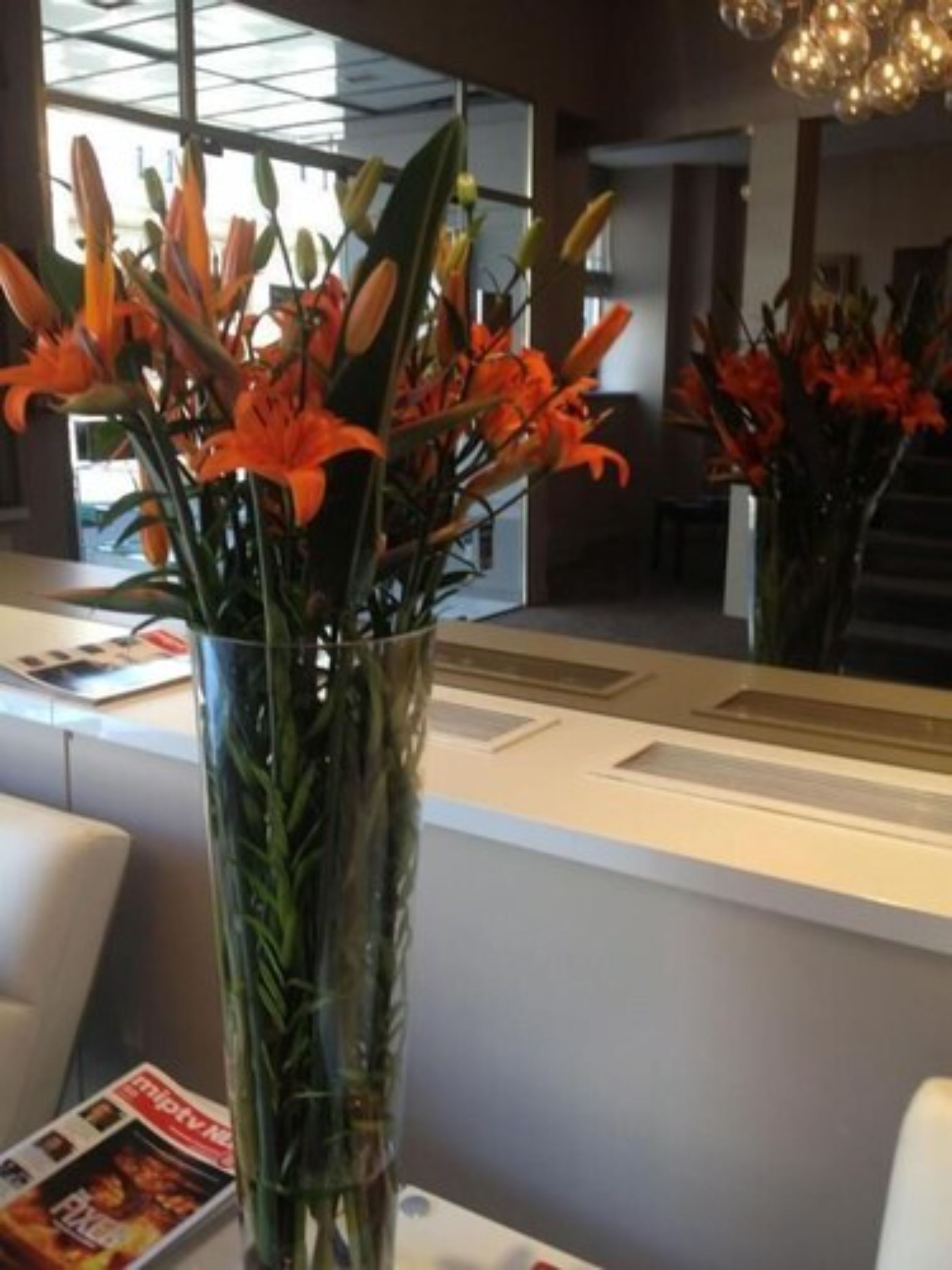 A reception area with a glass vase of orange lilies on a table, a magazine, and a modern interior design.
