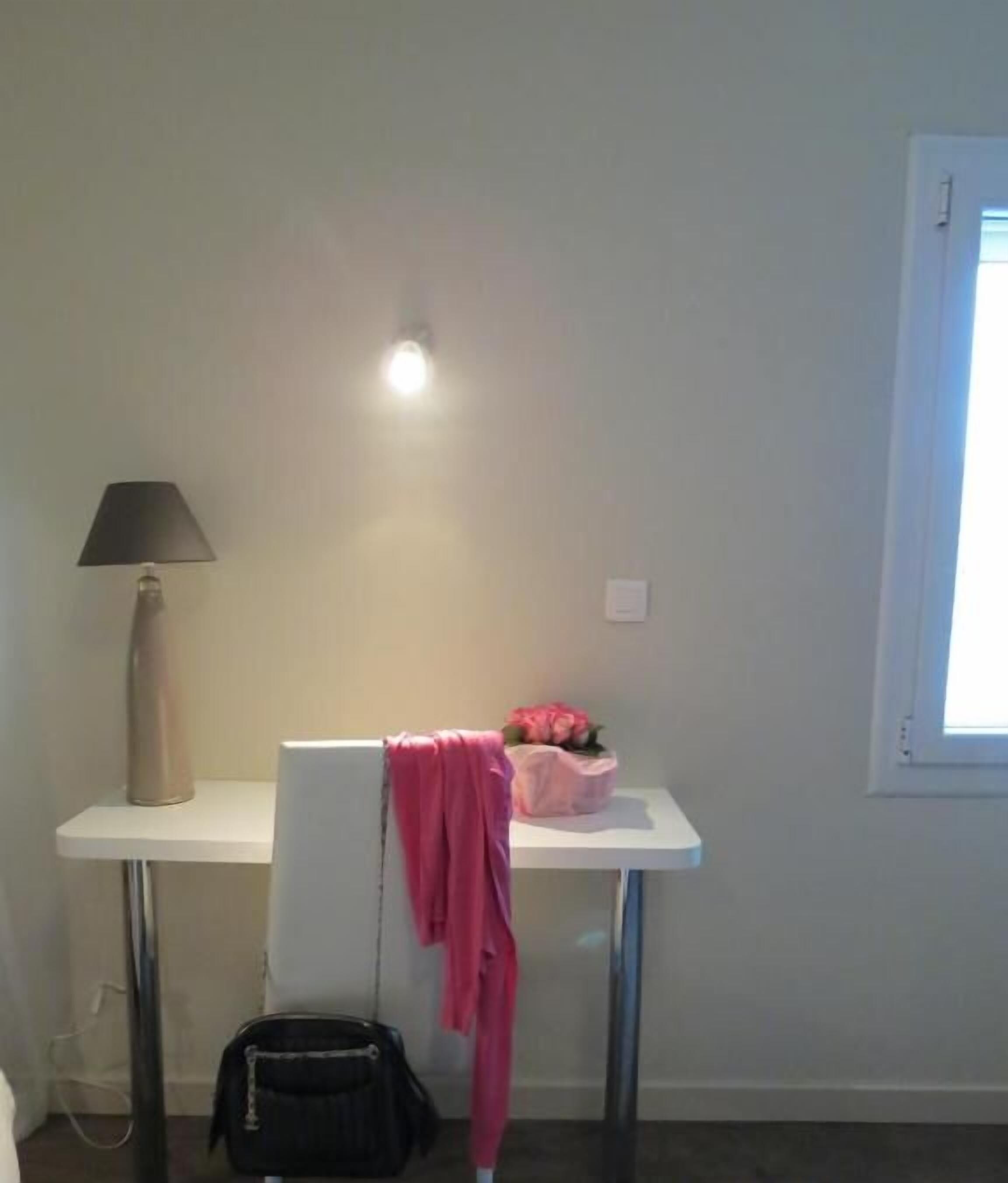 A small, simple room with a desk, a lamp, a chair, and a window.