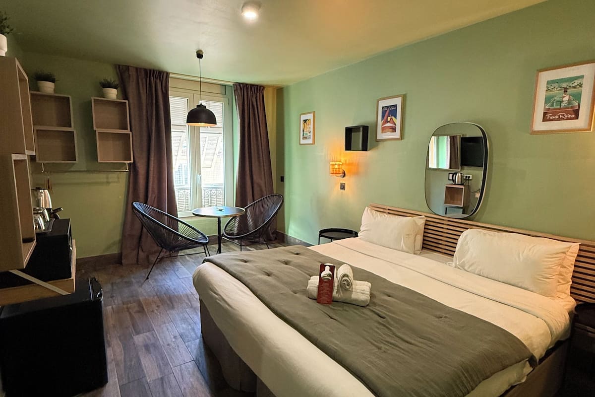 Una habitación de hotel con una cama grande, un escritorio, una silla, un armario y una ventana con cortinas.