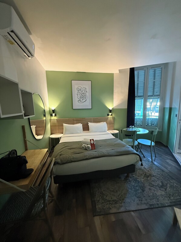 Una camera d'albergo con un letto, un comodino, uno specchio e un piccolo tavolo con sedie.