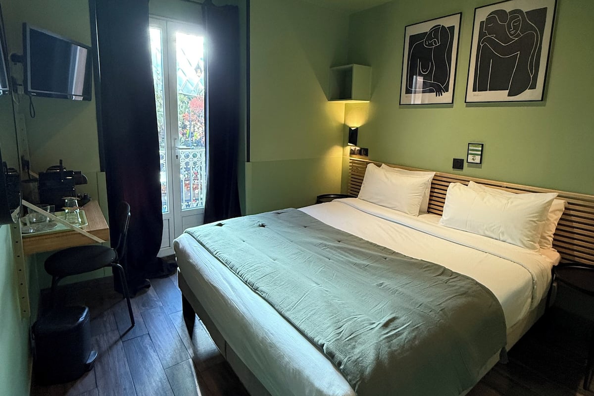Habitación de hotel con cama, escritorio, silla, televisor y obras de arte en la pared.