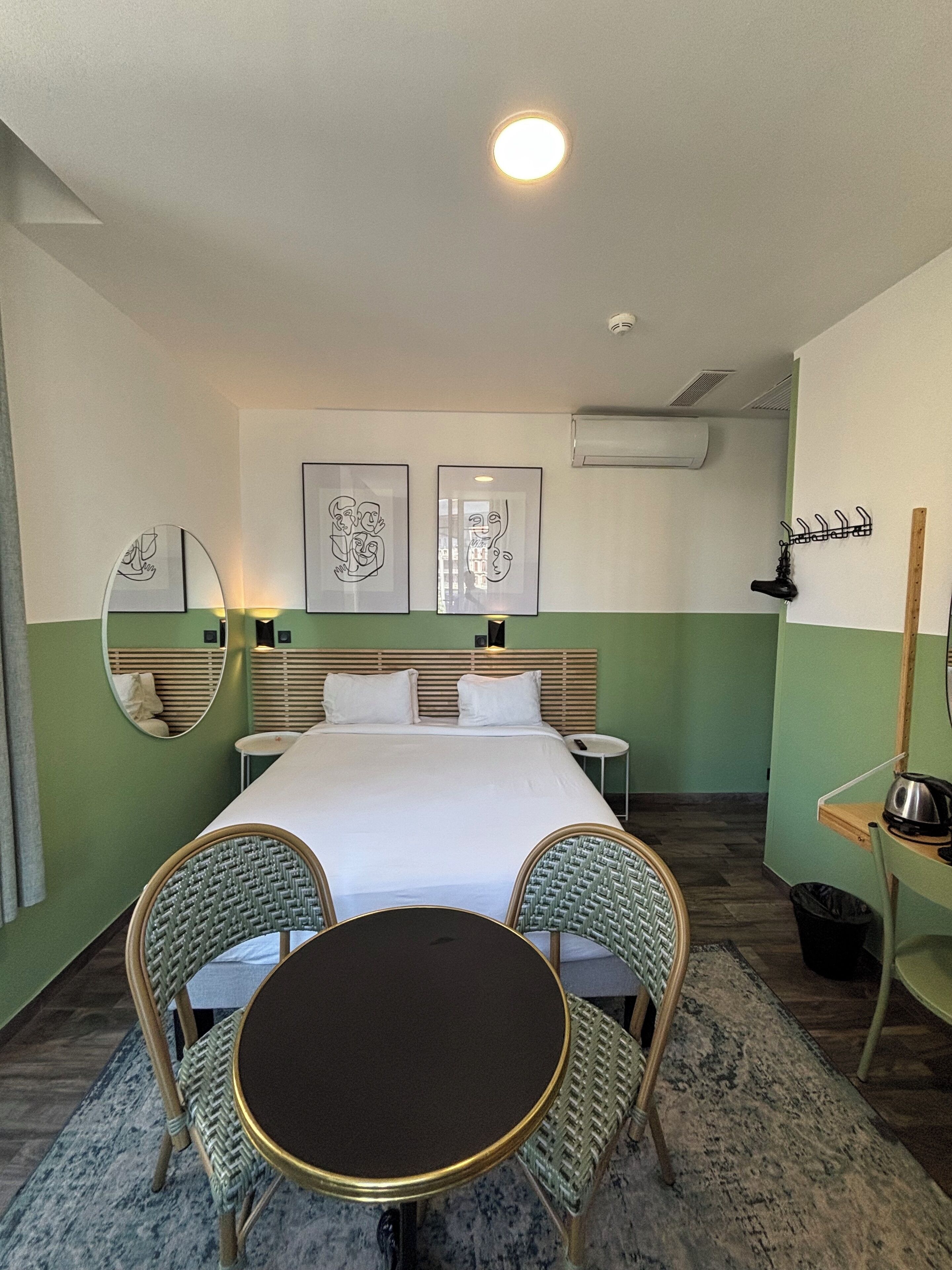 A hotel room with a bed, two chairs, a small table, and artwork on the walls.
