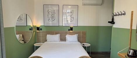 A hotel room with a bed, two chairs, a small table, and artwork on the walls.