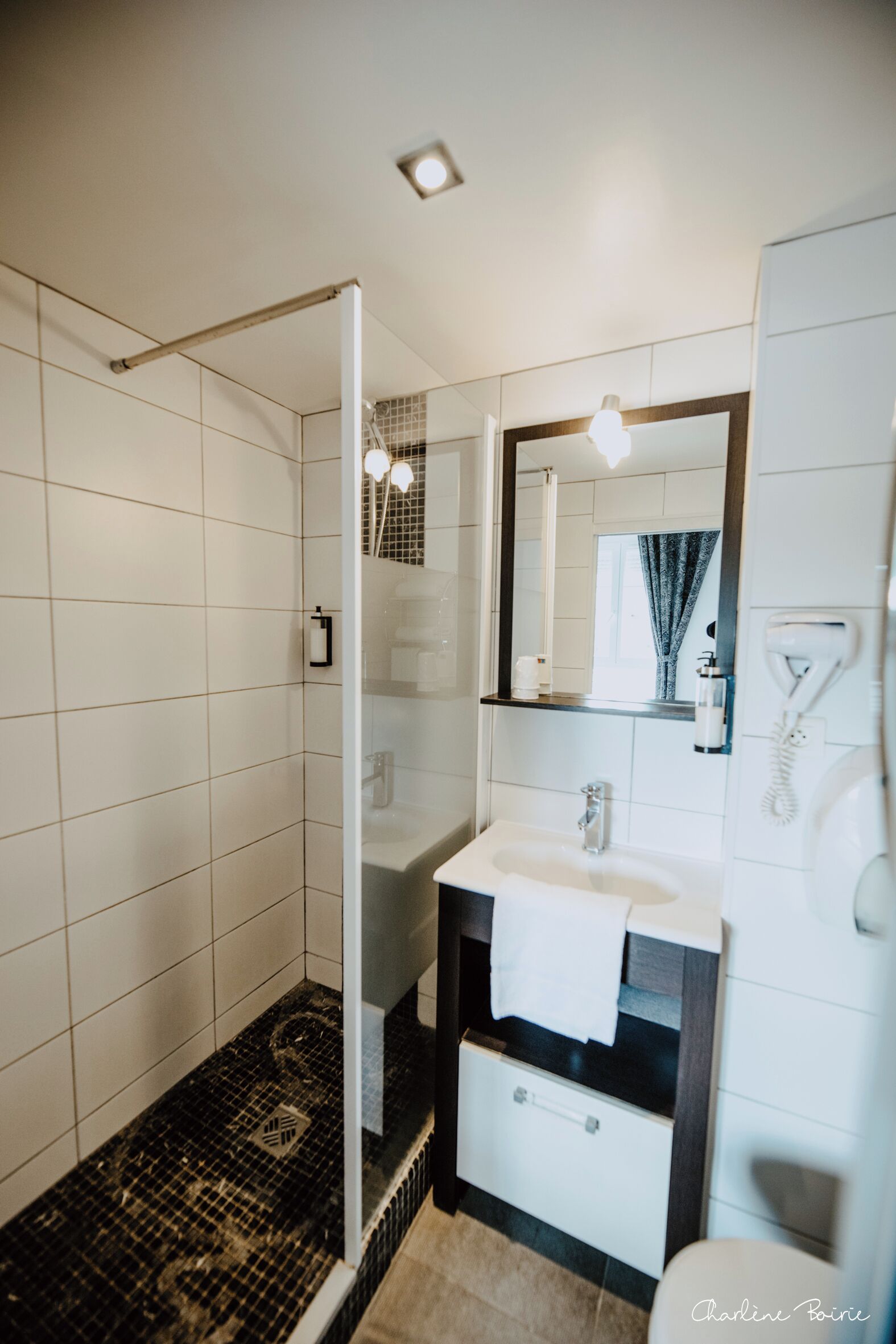 Un baño moderno con cabina de ducha de vidrio, un lavabo blanco con una toalla y un espejo sobre el lavabo.