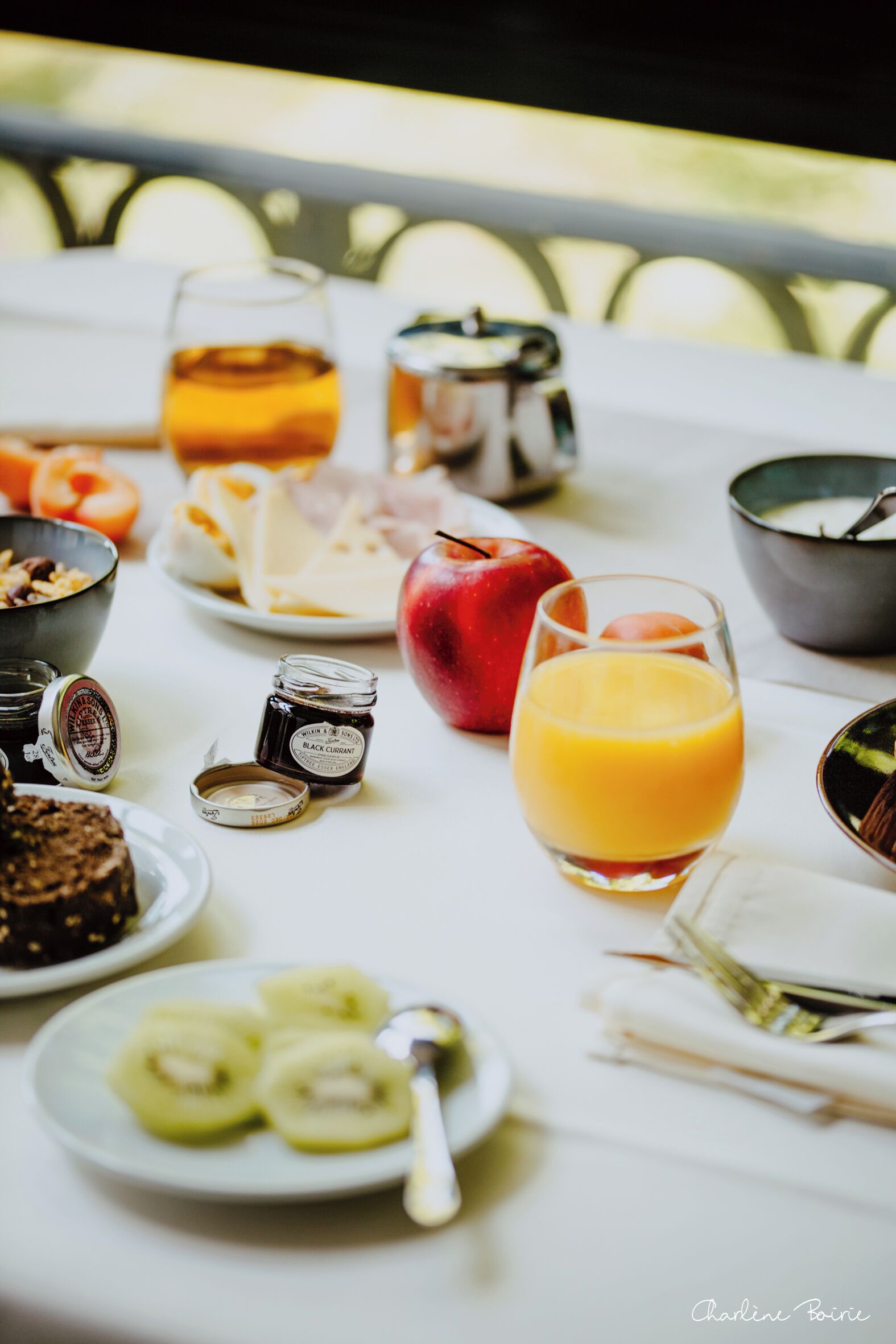 A breakfast table with various food items and drinks, including a glass of orange juice, a red apple, and sliced kiwi.
