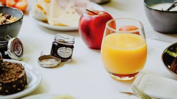 A breakfast table with various food items and drinks, including a glass of orange juice, a red apple, and sliced kiwi.