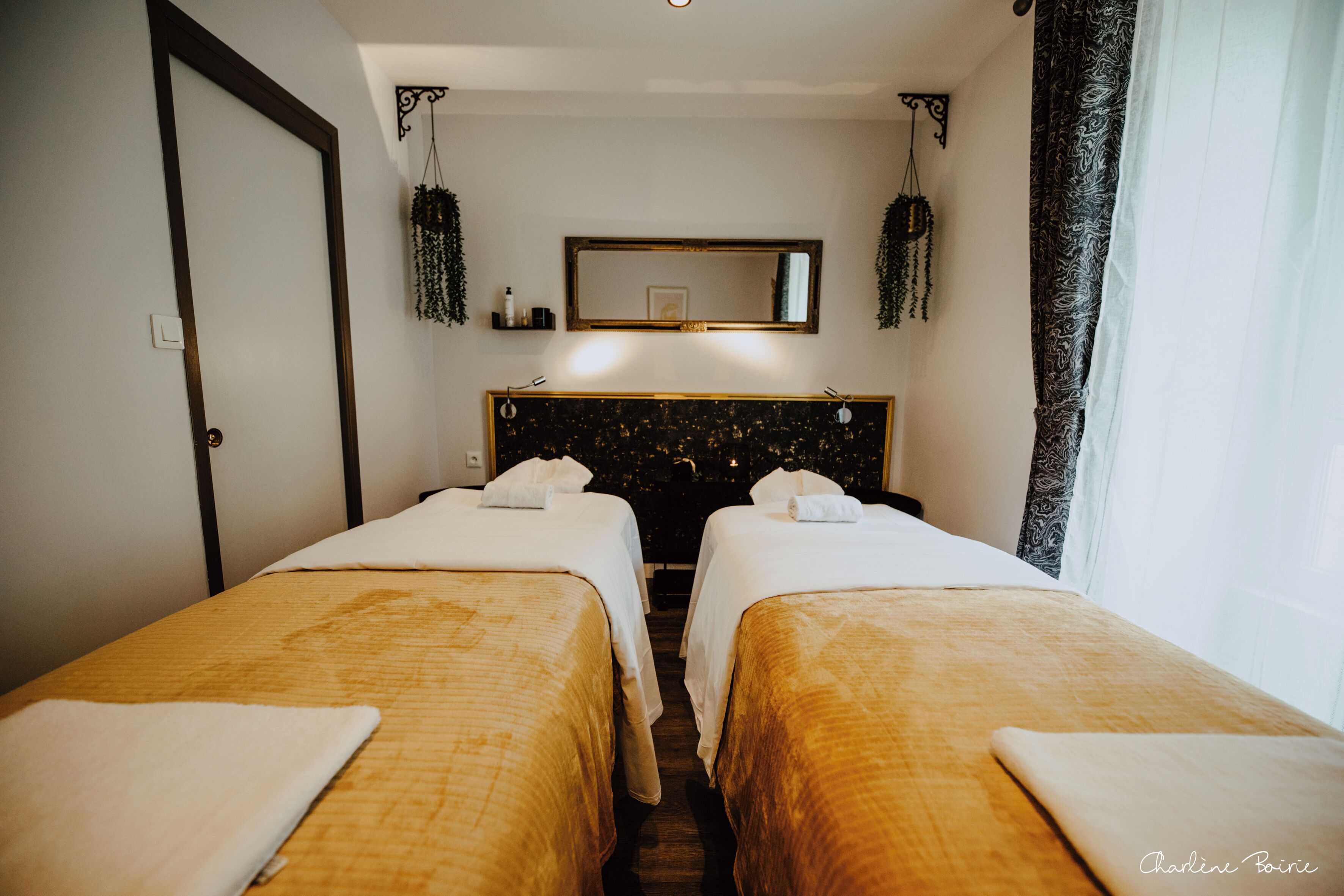 Habitación de hotel con dos camas individuales, un espejo grande sobre ellas y una ventana con cortinas.