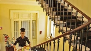 Una persona baja por una amplia escalera con balaustres ornamentados y barandilla, llevando una bandeja con comida.