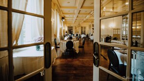 Un comedor de hotel con varias mesas y sillas, pisos de madera y ventanas amplias con cortinas.