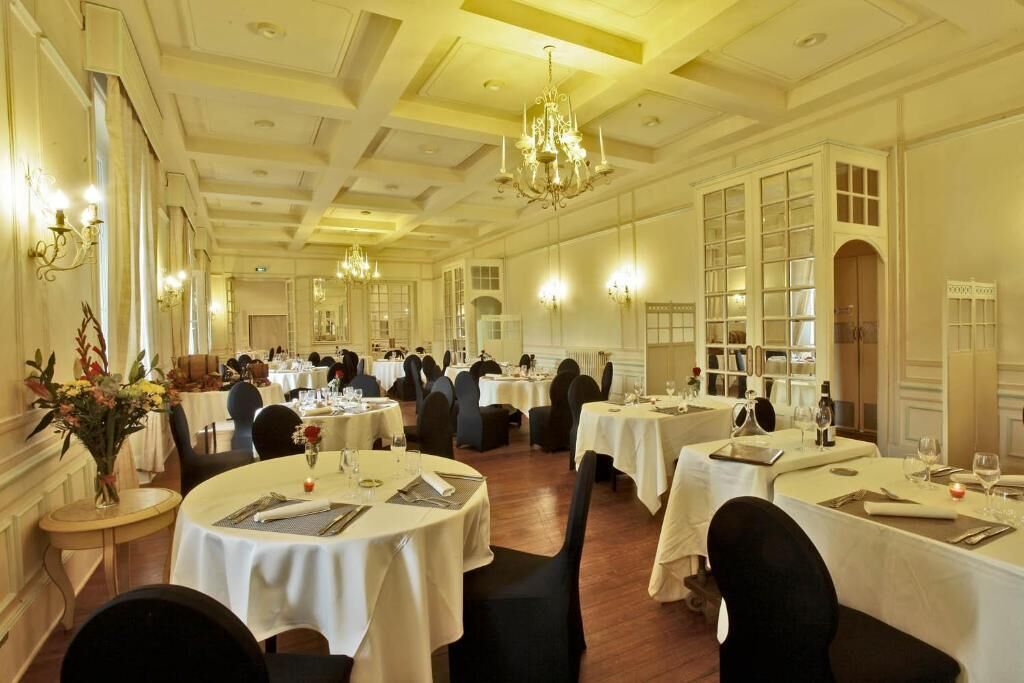 Une salle à manger élégante, avec des tables rondes, des lustres et des murs blancs.