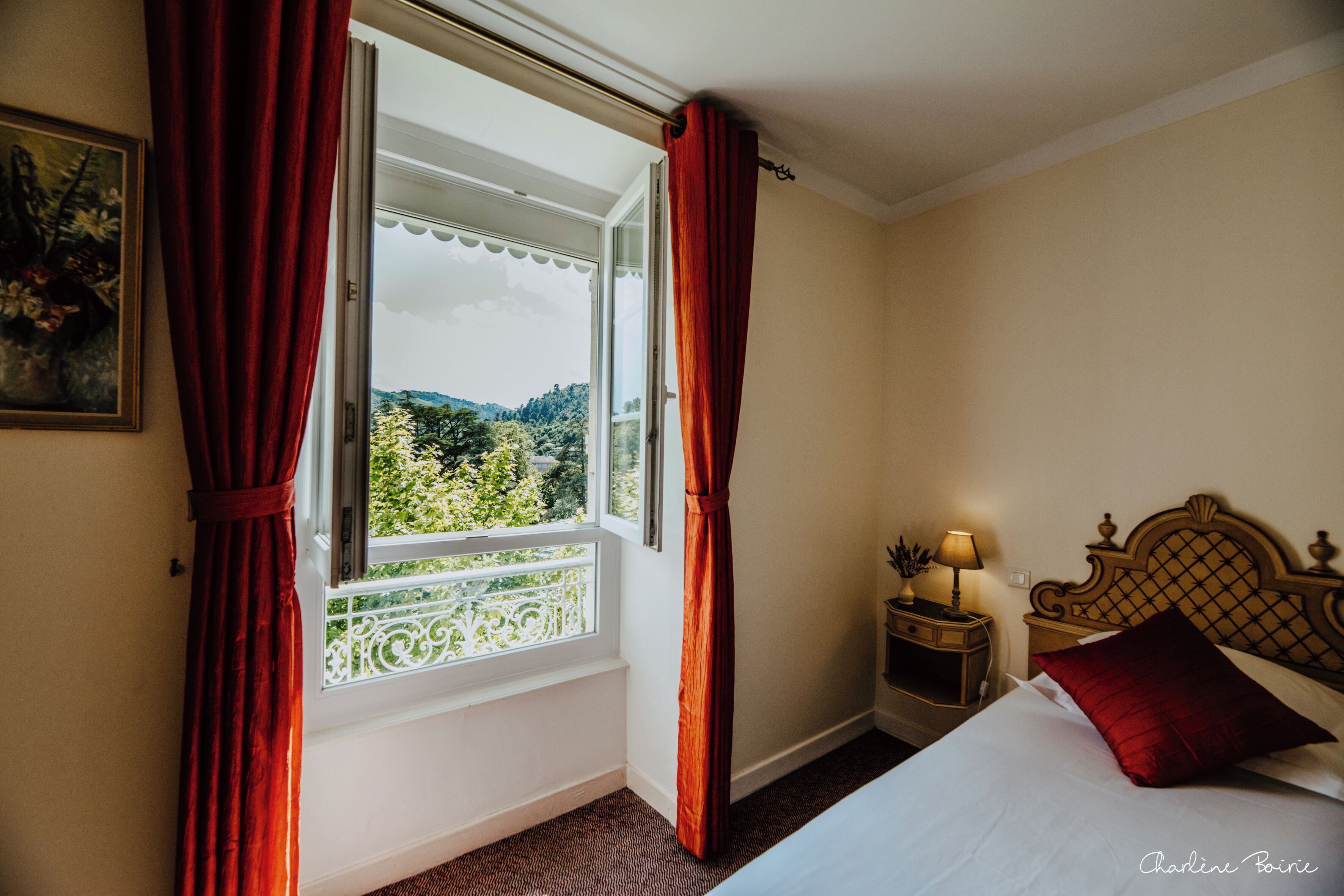 A hotel room with a bed, a nightstand with a lamp, and a window with curtains.