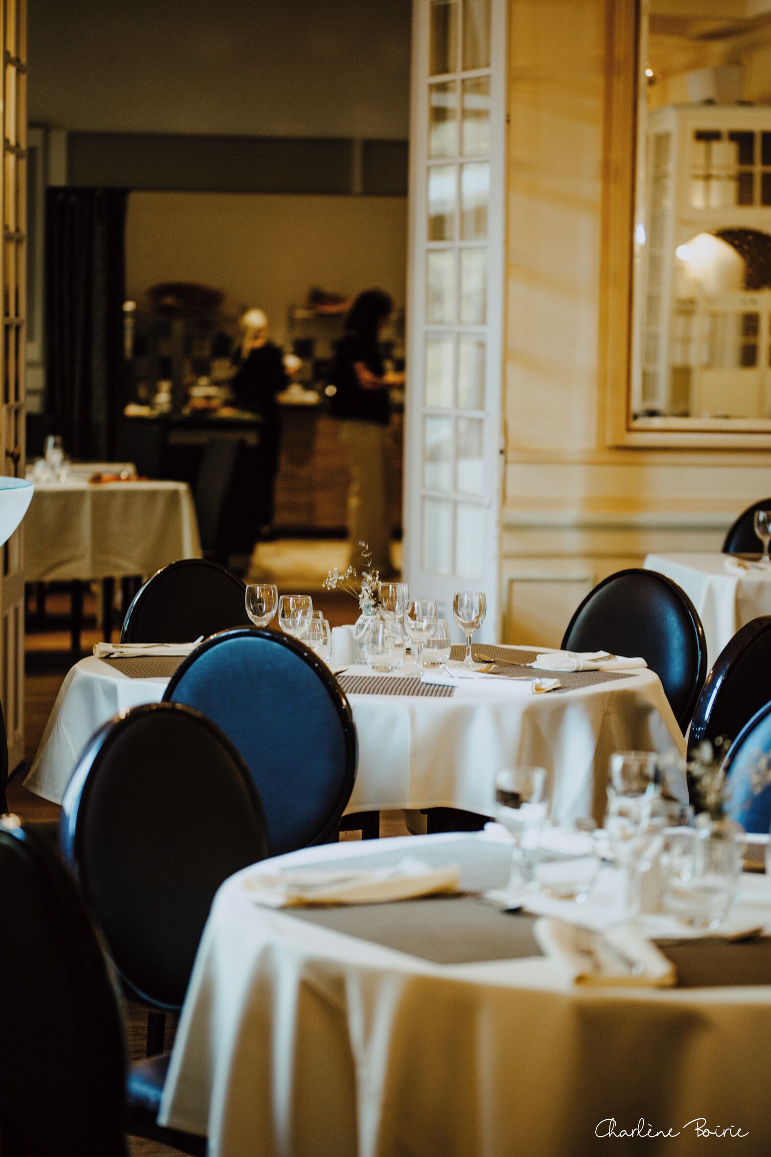 Un interno ristorante con tavoli apparecchiati, sedie e uno specchio a parete.