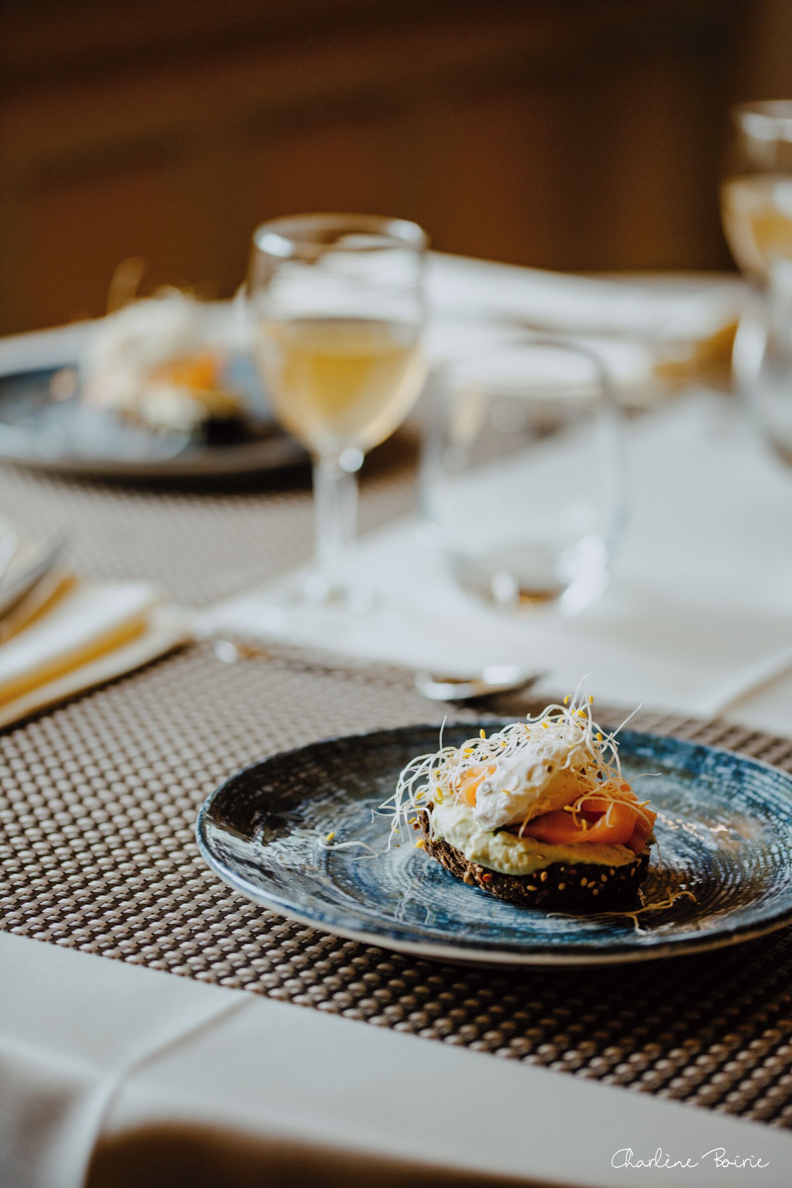 A dining table with a plate of food, a glass of white wine, and a napkin.