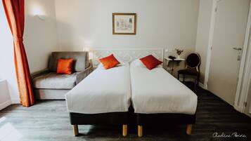 A hotel room with two single beds, a sofa, a chair, a small table, and a framed picture on the wall.