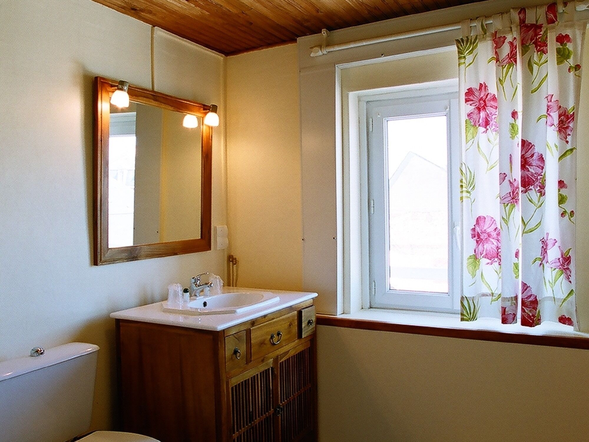 A bathroom with a wooden vanity, a mirror, a sink, and a window with floral curtains.