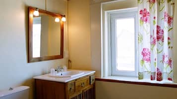 Une salle de bain avec un meuble-lavabo en bois, un miroir, un évier et une fenêtre agrémentée de rideaux à motifs floraux.