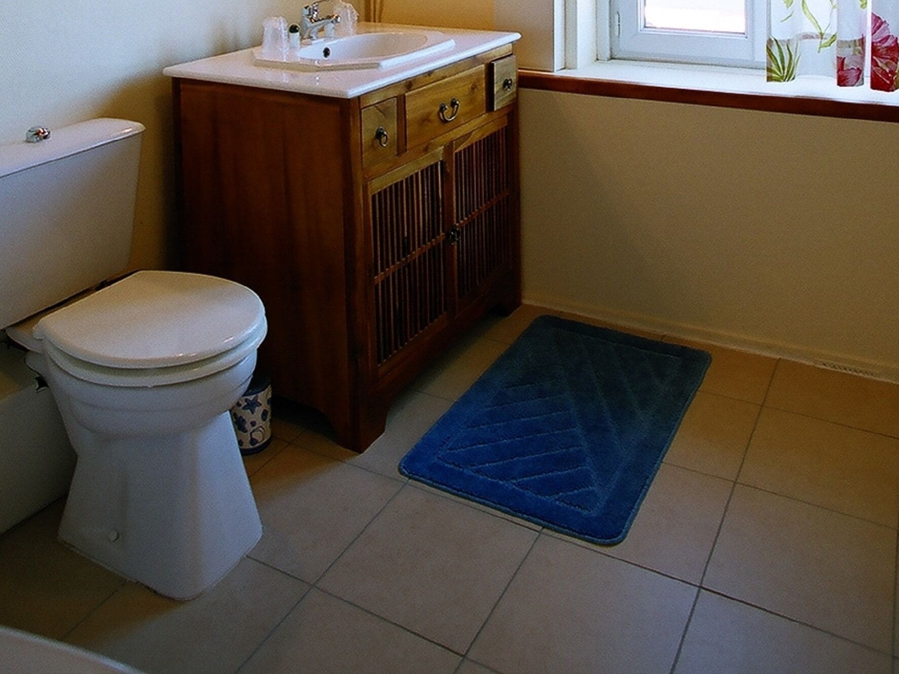 A bathroom with a toilet, wooden cabinet, sink, and a blue rug.