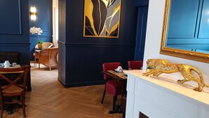 A modern living room with a fireplace, a dining area, and a large abstract painting on the wall. - The Originals Boutique, Hôtel d'Angleterre, Fécamp (Fecamp)