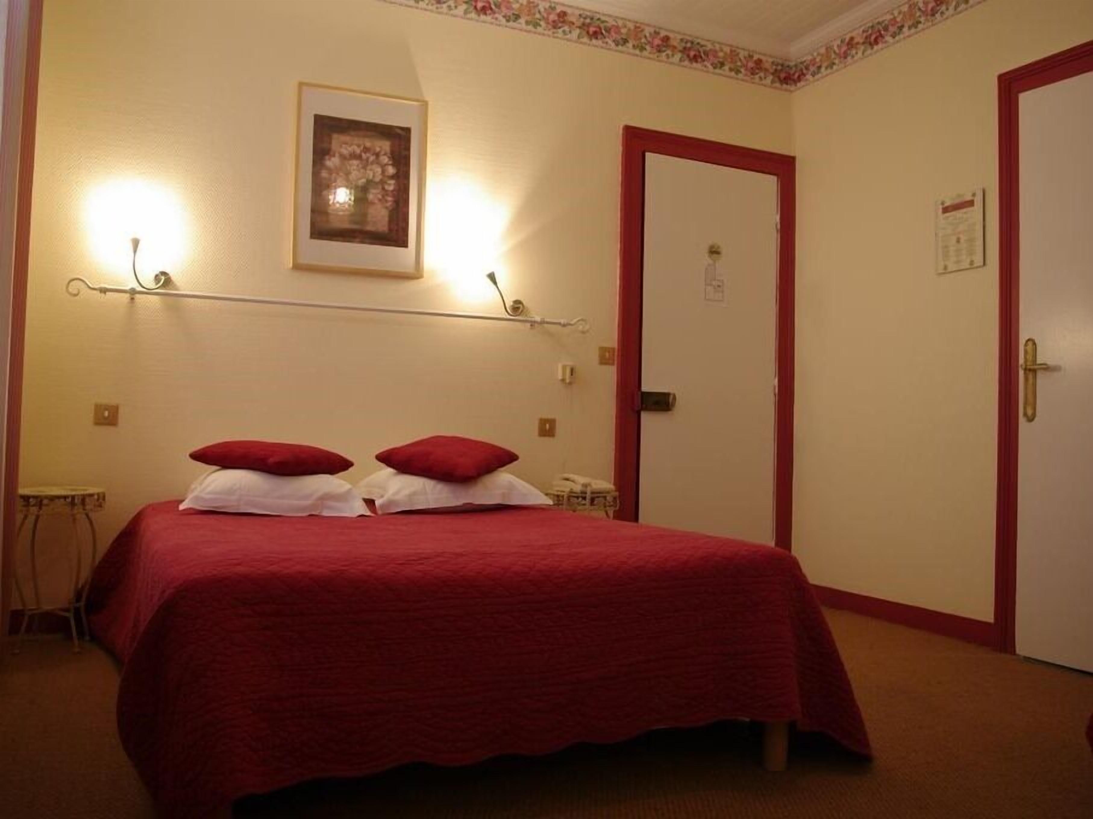 Habitación de hotel con cama, mesita de noche, silla, puerta y lámpara fijada a la pared.