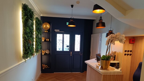 A modern interior with a dark door, wooden paneling, a blue chair, and a small reception desk with a plant. - The Originals Boutique, Hôtel d'Angleterre, Fécamp (Fecamp)
