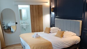 A modern hotel room with a large bed, a round table, a wooden accent wall, a mirror, and a dark headboard. - The Originals Boutique, Hôtel d'Angleterre, Fécamp (Fecamp)