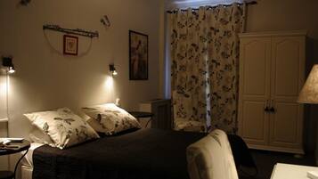 Un dormitorio con cama, mesitas de noche, una silla, armario y ventana con cortinas florales.