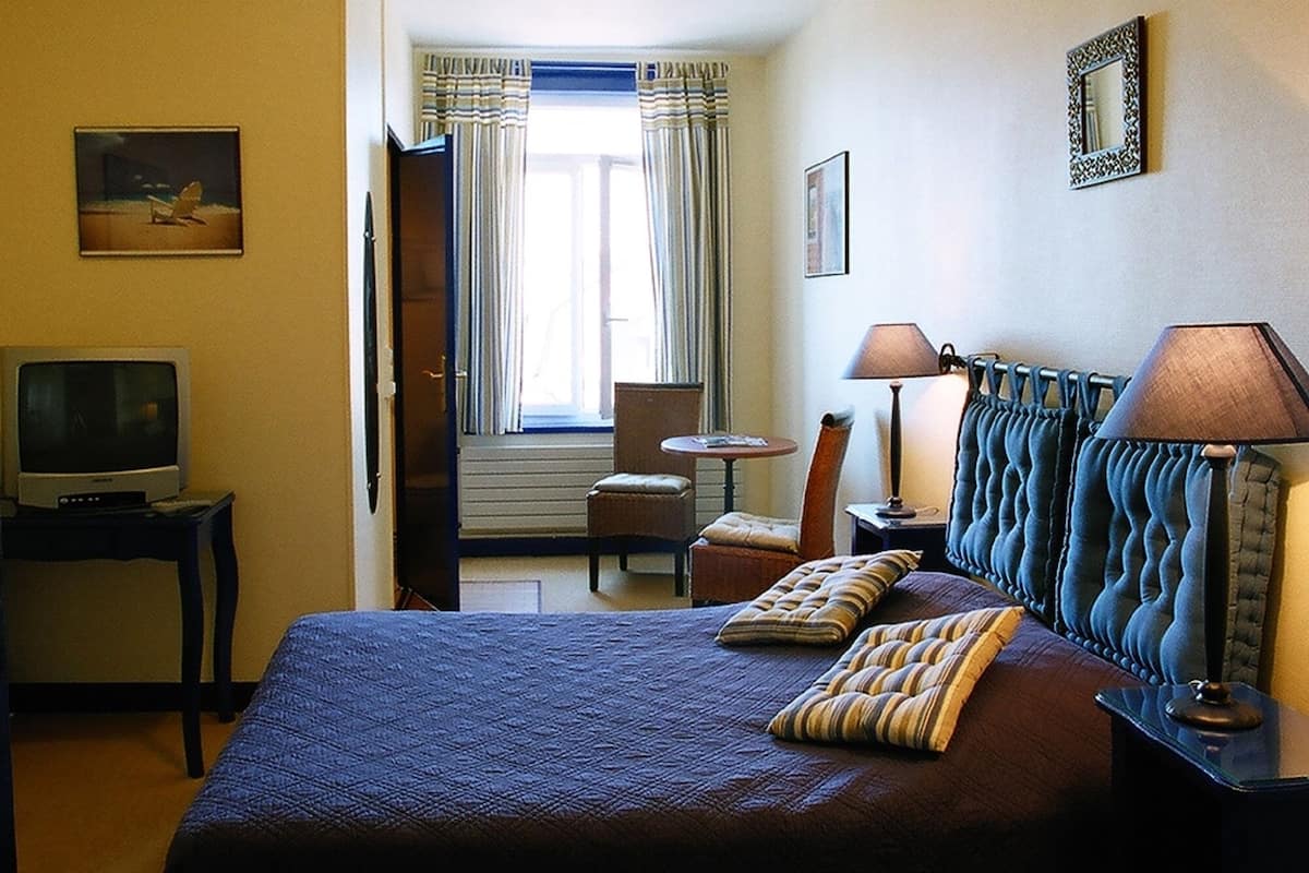 A hotel room with a bed, a television, a chair, a table, and a window with curtains.